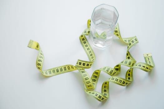 A glass of water is wrapped with a measuring tape on a white background. . High quality photo