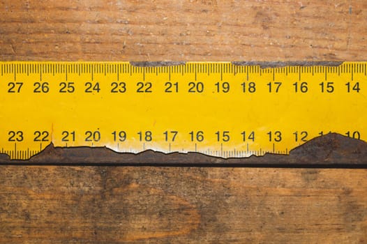 Old rusty yellow ruler with black numbers on a working wooden table. industrial background. carpentry workbench with copy space