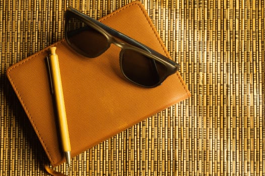 Diary and pen with sunglasses on a wooden bamboo background. notebook and pen top view. copy space