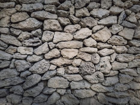 Irregular stone masonry wall background. Old limestone rocks of different size and shapes stacked carefully. Detailed texture of construction element. Antique rough manual work.