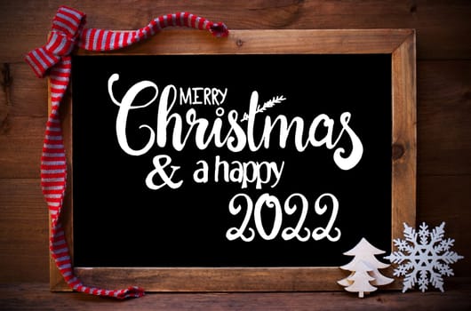 Chalkboard With English Calligraphy Merry Christmas And A Happy 2022. Christmas Decoration Like Tree, Snowflake And Bow. Wooden Background
