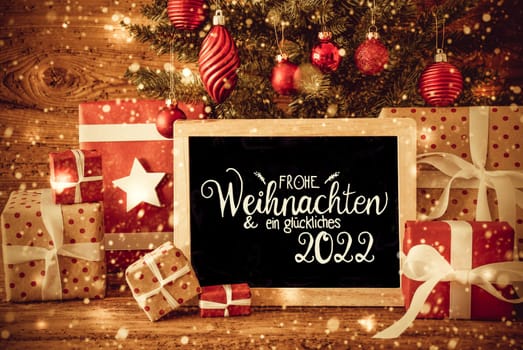 Blackboard With German Text Frohe Weihnachten Und Ein Glueckliches 2022 Means Merry Christmas And A Happy 2022. Christmas Tree With Decoration Like Ball, Gifts And Presents, Snowflakes