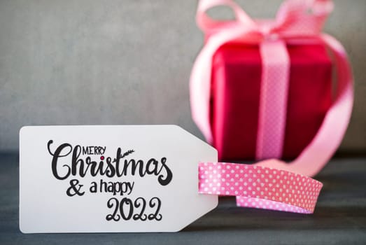 English Calligraphy Merry Christmas And A Happy 2022. Pink Present With Bow And Label. Gray Concrete Background