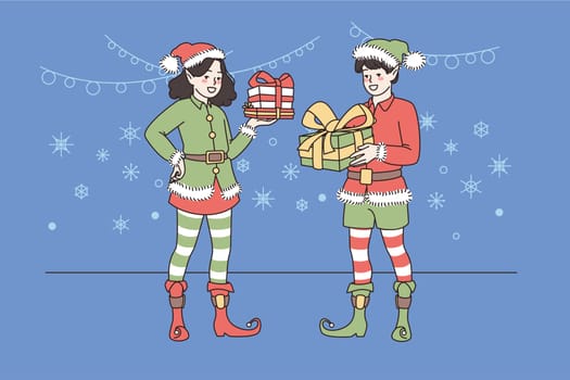 Smiling Santa helpers in festive costumes holding presents congratulate children on Christmas eve. Happy girl and boy elves with gifts greeting with New Year. Winter holiday. Vector illustration.