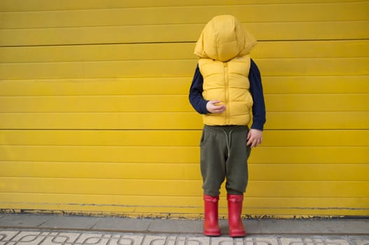 Little boy hides his face with his coat hood. Shyness on children concept
