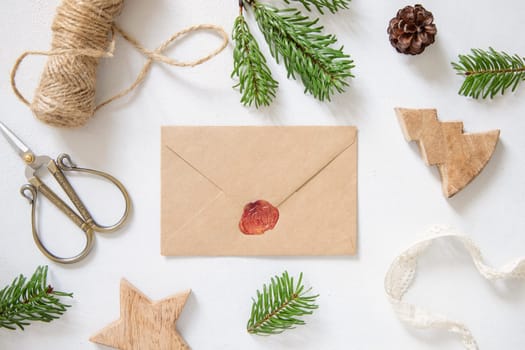 Winter Christmas Composition with a card over sealed envelope flat lay. Christmas and New Year greeting card template with fir tree branches and pine cones on white wooden background top view. Holiday mockup.