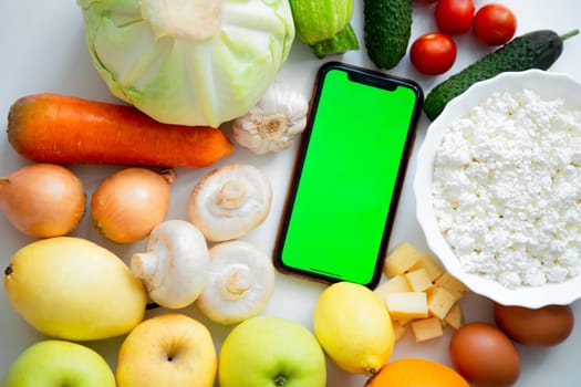 A phone with a green screen lies among fruits, vegetables and dairy products. High quality photo