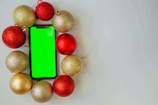 A phone with a green screen lies among the golden and red Christmas balls. High quality photo