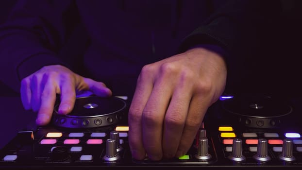 DJ plays music. sound mixer controller with knobs and sliders close up. hands on the mixing deck with turntables at dark with illuminated controls