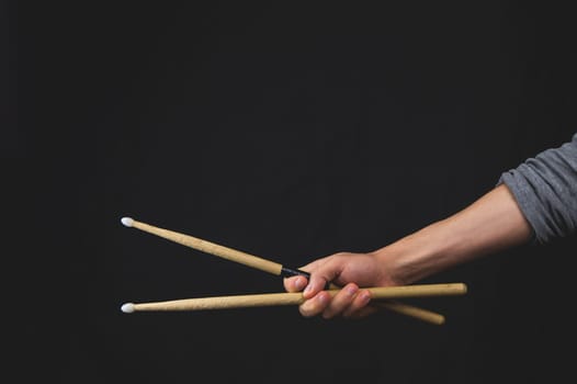 Hand holds wooden drumsticks in the dark. copy space