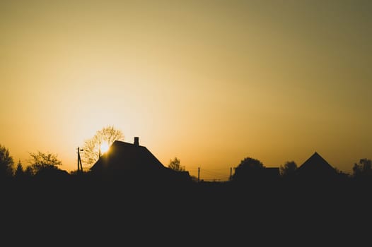 Silhouette of houses with trees at sunset. sun setting behind the forest. evening landscape