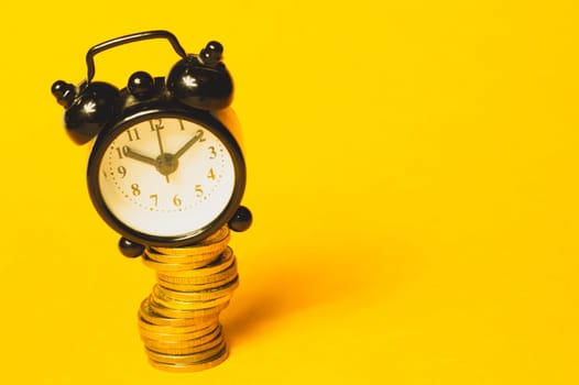 Time is money concept. classic alarm clock with coins on yellow background. vintage watch with round dial. copy space