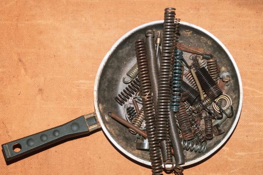 Metal rusty springs in a frying pan on a wooden background. industrial concept. work tool. copy space