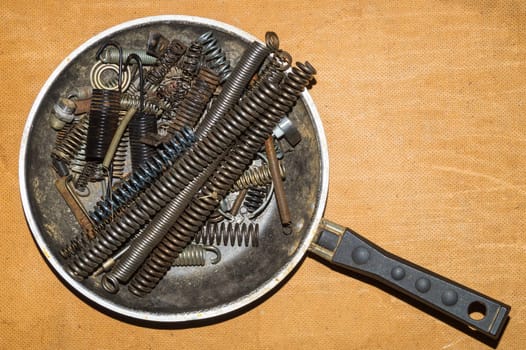 Metal rusty springs in a frying pan on a wooden background. industrial concept. work tool. copy space