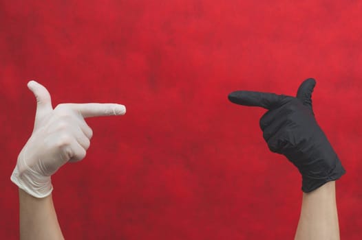 Hands in protective gloves point finger at each other. one hand in black glove, other in white. gesturing hands in surgical gloves on a red background