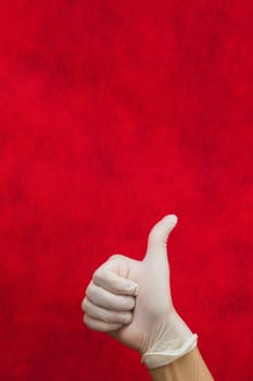 Hand in white medical glove shows thumbs up on a red background
