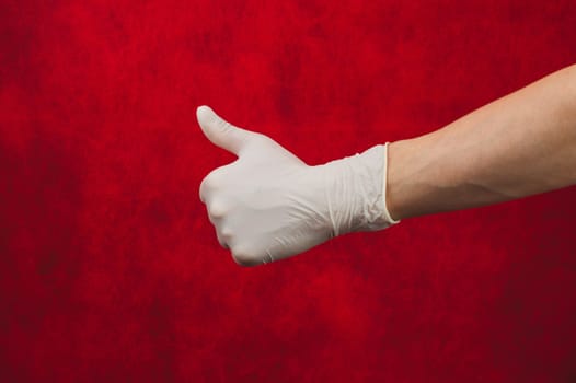 Hand in white medical glove shows thumbs up on a red background