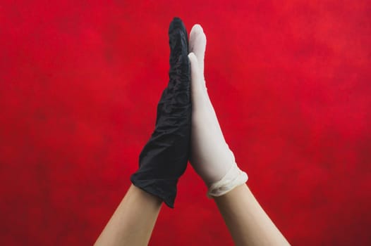 High five in protective gloves on a red background. one hand in black glove, other in white. gesturing hands in medical gloves