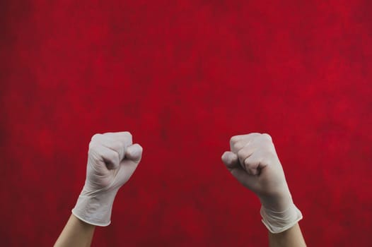 Hands in medical gloves clenched into fists. gesturing hand in white protective gloves on a red background