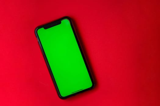 A phone with a green screen is on a red background. High quality photo