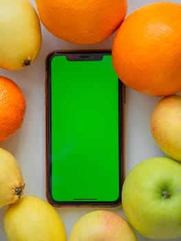 A phone with a green screen is lying among the fruits. High quality photo