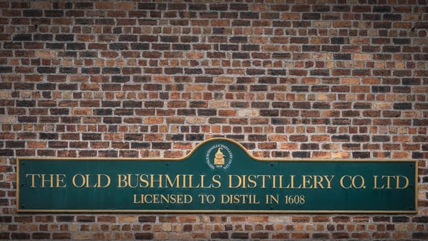 Bushmills, Northern Ireland, Aug 2019 The Old Bushmills Distillery Co. Ltd Licensed to distil in 1608 sign on rustic brick wall