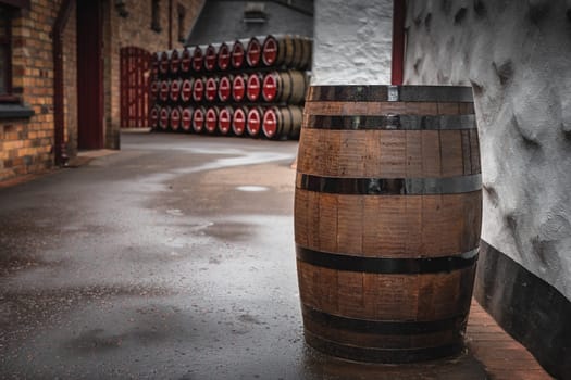 Old, vintage wooden whiskey barrel in an alley with rows of barrels in background, Bushmills town, Antrim, Northern Ireland