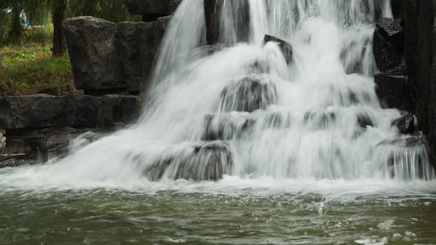 Small waterfall flows into a pond. rushing stream water background