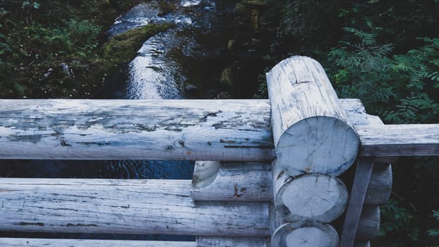 Detail of wooden bridge fencing made of logs. river on background