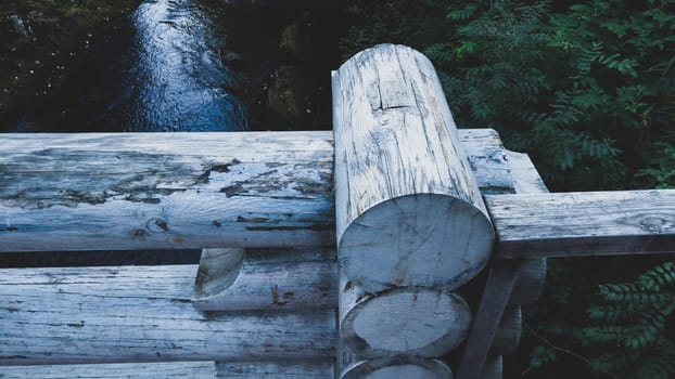 Detail of wooden bridge fencing made of logs. river on background
