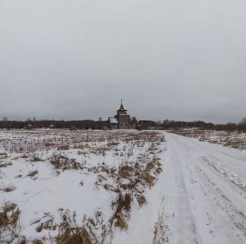 Wooden church in the middle of winter field. traditional building far away. snowy road
