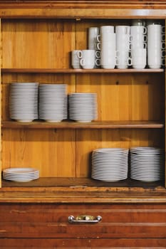 Vintage cupboard with white dinnerware. old wooden kitchen cabinet with stack of white plates and cups. retro sideboard