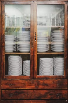 Vintage cupboard with white dinnerware. old wooden kitchen cabinet with stack of white plates and cups. retro sideboard