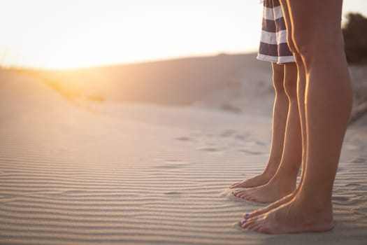 side view closeup of young woman and her child feet standing on sand dunes at sunrise