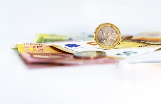 A used 1 euro coin standing on top of some euro banknotes. Economics and finance in the European Union.