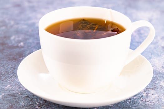 Steeping a herbal tea bag in a porcelain cup close up