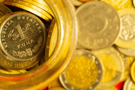 Coins of different countries in a glass jar. a lot of metal coins of different denominations and various countries. financial background. croatian kuna in the foreground