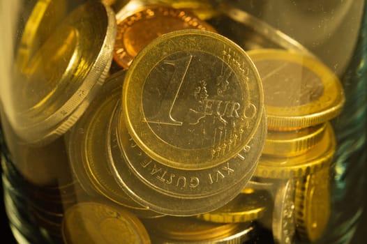 Coins of different countries in a glass jar. a lot of metal coins of different denominations and various countries. financial background. euro coin in the foreground