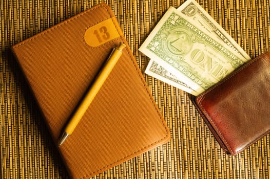 Dollars in a wallet with a notebook and pen. money on wooden bamboo background. finance background