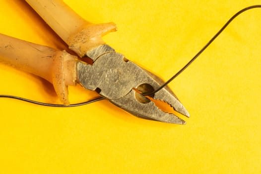 Pliers cuts a black wire on yellow background. pliers with orange handles. work tool. copy space
