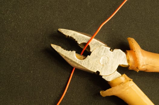 Pliers cuts a red wire on black background. pliers with orange handles. work tool. copy space