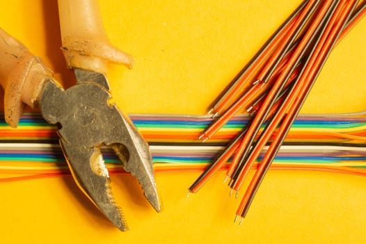 Pliers and colorful wires on yellow background. work tool