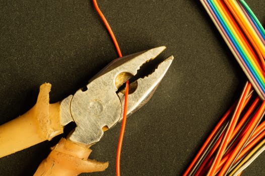 Pliers cuts a red wire on black background. pliers with orange handles and colorful wires. work tool. copy space