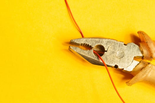 Pliers cuts a red wire on yellow background. work tool. copy space