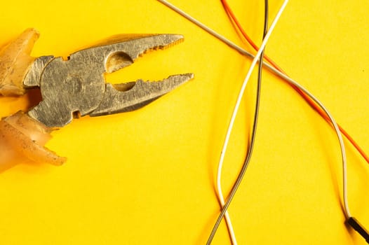Pliers and colorful wires on yellow background. work tool