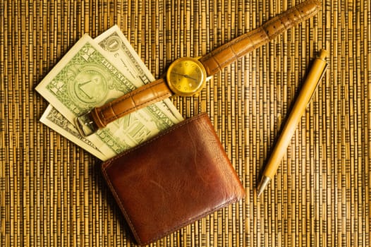 Dollars in a wallet with a gold wristwatch and pen. money on a wooden bamboo background. financial background