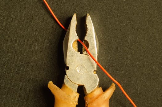 Pliers cuts a red wire on black background. pliers with orange handles. work tool. copy space