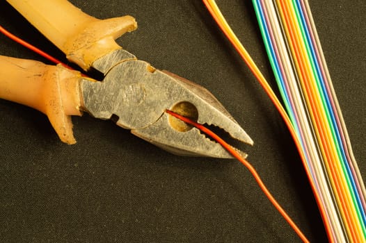 Pliers cuts a red wire on black background. pliers with orange handles and colorful wires. work tool. copy space