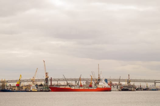 Red cargo ship in the harbor. bridge over the river with industrial works. many industrial cranes in the port