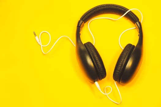 Black headphones with white cable on a yellow background. modern earphones